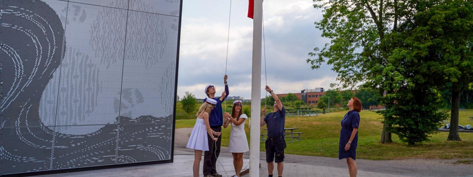 De tre studenter hejser flaget sammen med rektor