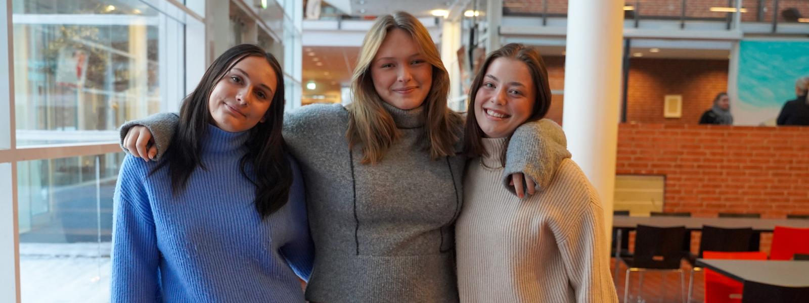 Tre smilende piger holder om hinanden i kantinen