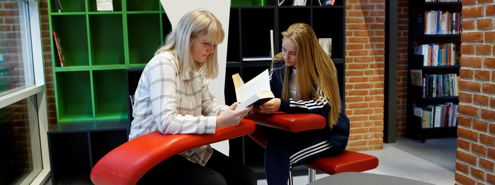 To piger sidder og læser i en rød stol i Studiecentret